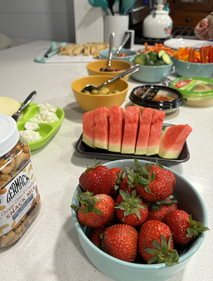 A spread of food including nuts, strawberries, watermelon, cheese, hummus, cut veggies, bread and crackers. 